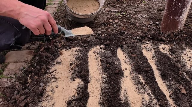 Hand preparing soil beds with rows of earth for planting in garden outdoors.
