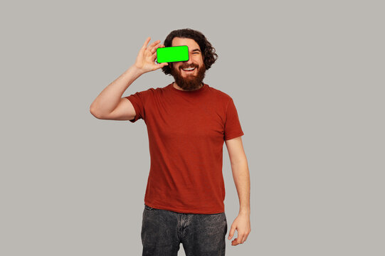 Caucasian Man Holding Green Phone To Eye, Playful Peek And Experimental Framing, Red Shirt And Beard, Studio