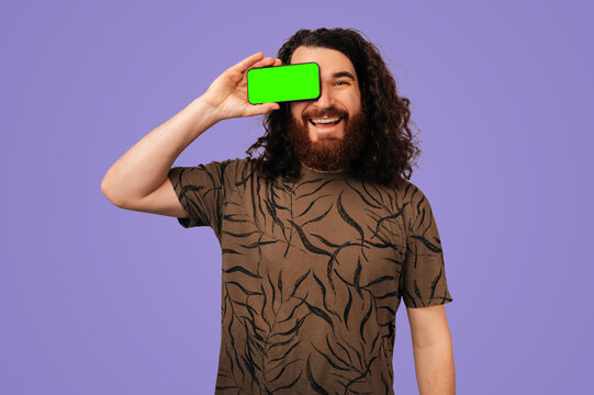 Smiling Man Hiding Eye With Green Card, Studio Portrait On Purple Background, Playful Mockup Demo For App