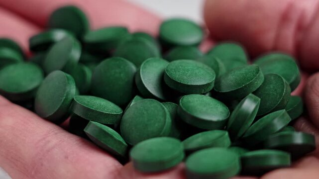Green spirulina pills poured into a patient hand. Macro shot