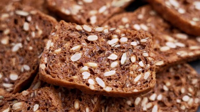 Crunchy whole grain toast falling onto a heap of rye crackers. Dark toasted bread with sunflower and pumpkin seeds. Slow motion