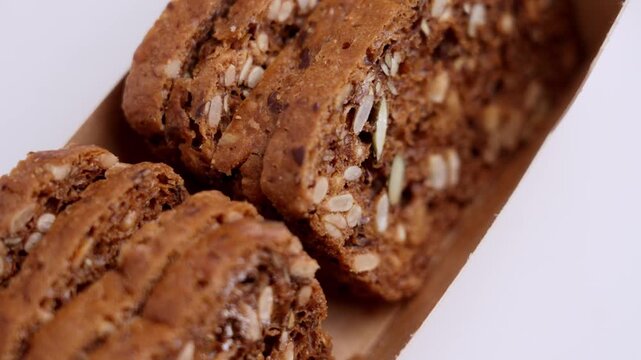 Crispy artisan crispbread slices arranged in a brown kraft paper box. Dark grain bread filled with sunflower kernels and pumpkin seeds. Rotation