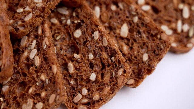 Slices of dark multigrain crispbreads or gluten-free toasts with sunflower and flax seeds on ceramic plate. Top view. Rotation