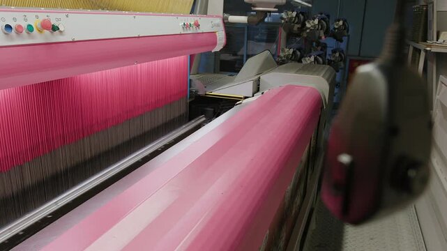 Automated industrial loom manufacturing fabric with pink and black threads in a textile factory