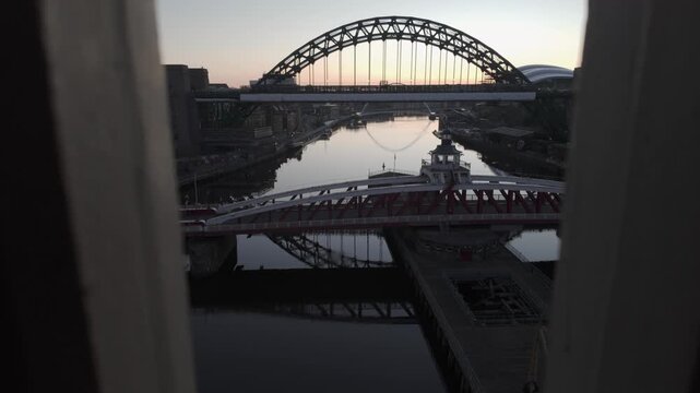 Aerial predawn view through a foreground frame toward the River Tyne in Newcastle, featuring the Swing Bridge and Tyne Bridge with the Millennium Bridge and The Glasshouse in the distant background.