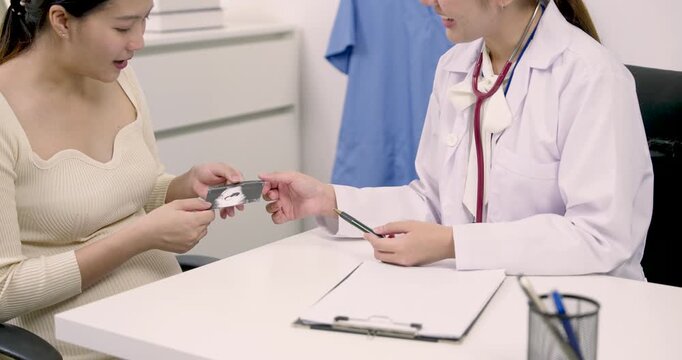 Pregnant Asian woman expressing emotion while holding ultrasound photo during conversation with female obstetrician showing personal bonding and trust during third trimester prenatal consultation