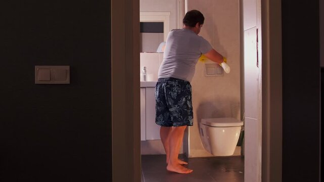 Man spraying cleaner from plastic bottle onto tiled wall in bathroom, cleaning surface at home, hygiene routine, removing dirt and stains, household maintenance and sanitation concept