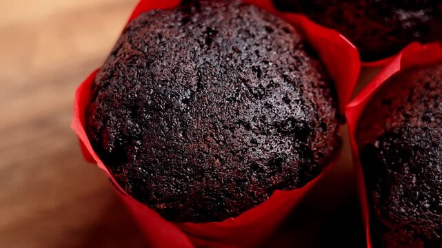Dark chocolate muffin in a red paper wrapper on a wooden table. Concept of festive treat. Rotation