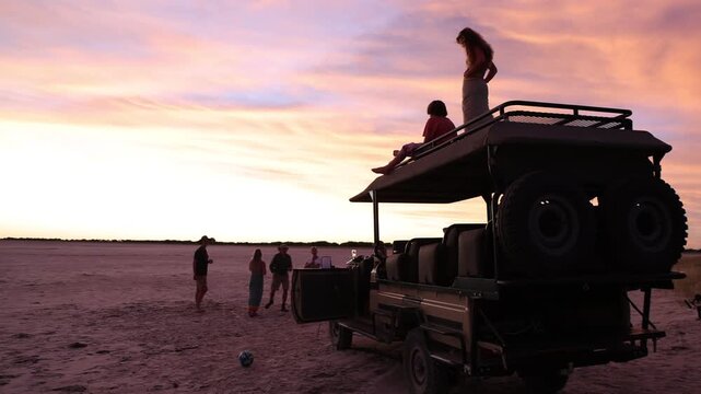 brother and sister atop safari vehicle looking at sunset, Makgadigadi National Park, Botswana, Africa
