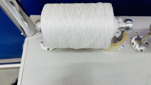 White packing rope spool on counter, metal dispenser and tape roll nearby, clean white surface, closeup texture of fiber coil