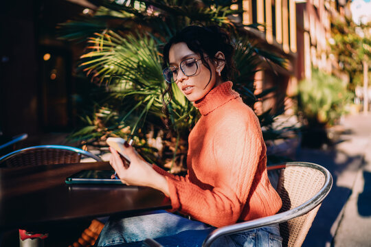 Confident multiracial woman holding smartphone and stylus at outdoor terrace, digital nomad checking notifications, mobile banking and online shopping concept, modern business communication.