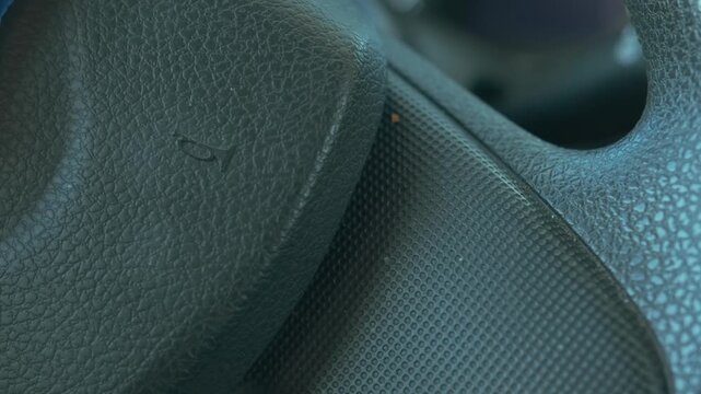 Close-up of car steering wheel horn area being pressed inside modern vehicle interior, sound signal control without hands visible, safety alert feature in car driving environment (