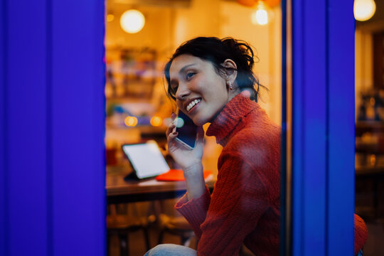 Portrait of happy hispanic girl having phone call in city cafe at night, using smartphone for mobile communication and networking, digital nomad lifestyle, authentic representation, copy space.