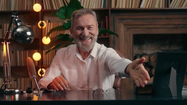 Happy smiling Caucasian old aged senior business man inviting sit at chair in office friendly cheerful retired male businessman taking off glasses invite sitting at table welcome meeting interview