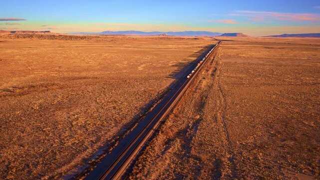 Cinematic drone aerial of massive freight train traveling through western landscape, desert terrain, rail transport, logistics industry