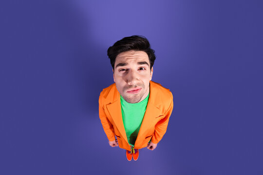 Young man in colorful outfit looking up in overhead portrait on purple background with quirky expression and bold orange blazer