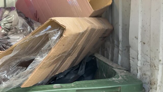 Close-up overflowing green dumpster loaded cardboard and construction debris including insulation, taped bags, crushed packaging