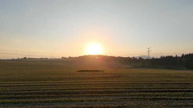 Horizontal Wide-Angle View of a Harvested Agricultural Field at Sunset with an Electrical Pylon and Hazy Horizon