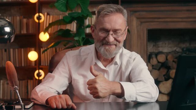 Caucasian aging retired old business man looking at photo at table showing thumb up look at camera recommending gesture at home office agency aged male executive senior businessman excited hand sign