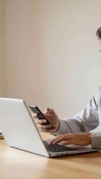 Vertical video: Starting work, person in gray top raising phone and typing on laptop at home desk
