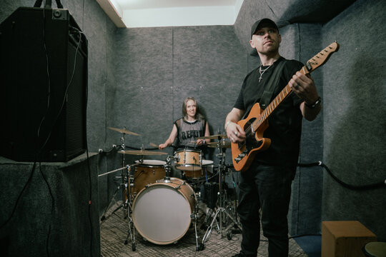 Male guitarist with female drummer in rehearsal room band practice. Rock music teamwork, instrument playing and creative session.