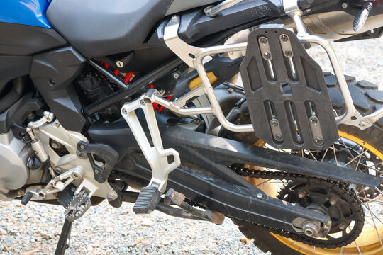 Close up detail of modern adventure motorcycle showing suspension swingarm chain footpeg luggage rack frame and tire parked outdoors waiting for exciting offroad travel