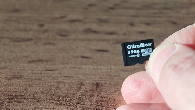 Sosnoviy Bor, Russia - April 21, 2026: MicroSD memory card held between fingers, displaying brand name OltreMax and storage capacity of 32GB on a wooden surface