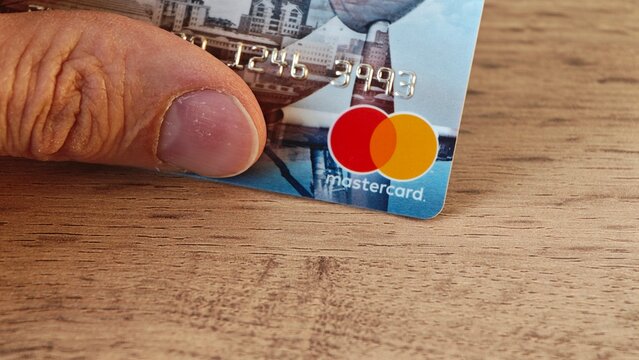 Sosnoviy Bor, Russia - April 21, 2026: Close-up of a hand holding a Mastercard credit card with visible logo and card details on a wooden surface