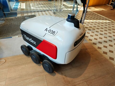 Sankt Petersburg, Russia - March 19, 2026: Yandex delivery robot with six wheels positioned indoors on a wooden floor, showcasing a modern design and technology features
