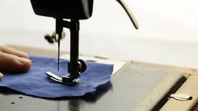 A seamstress works on a vintage sewing machine, sewing blue fabric