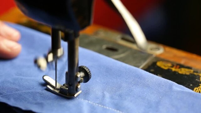 A seamstress works on a vintage sewing machine, space for text, sewing blue fabric