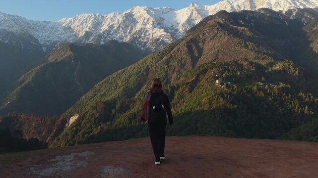Woman walking on mountain viewpoint raising arms as drone flies backward over landscape.