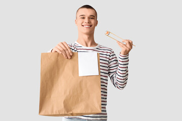 Young man with tasty sushi and paper bag on light background © Pixel-Shot