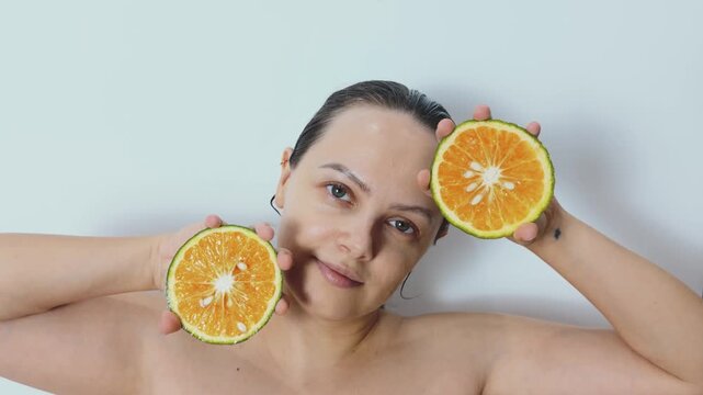 Woman holding two sliced oranges near her face, representing natural skincare, vitamin c benefits, and promoting self care with natural ingredients for healthy, radiant beauty