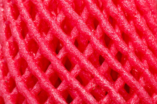 Bright red foam net packaging wrapper texture macro photography showing intricate mesh pattern over vibrant pink background creating abstract textured surface