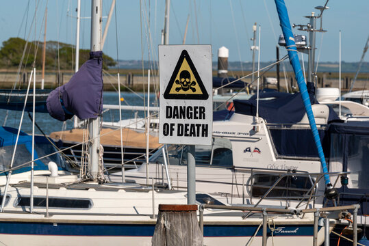 Lymington River Hampshire England UK. 25.04.2026.  A stark warning sign featuring a skull and crossbones symbol is prominently displayed amidst a backdrop of docked sailboats and yachts