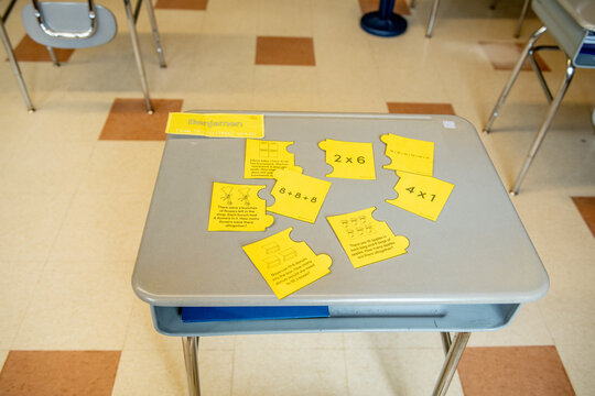 Yellow flash cards or activity cards are scattered across a student desk in an elementary classroom, a hands-on learning activity in progress.
