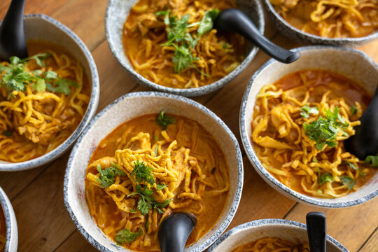 Bowls of khao soi northern Thai coconut curry noodle soup with chicken garnished with cilantro served on wooden table offering warm inviting and appetizing culinary experience for food lovers
