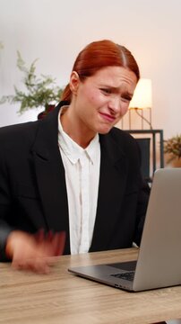 Young businesswoman at home office sees laptop screen freeze slaps table grabs head stressed. Freelancer girl at table hits ctrl alt del waits anxious hoping system recovers soon to keep working again
