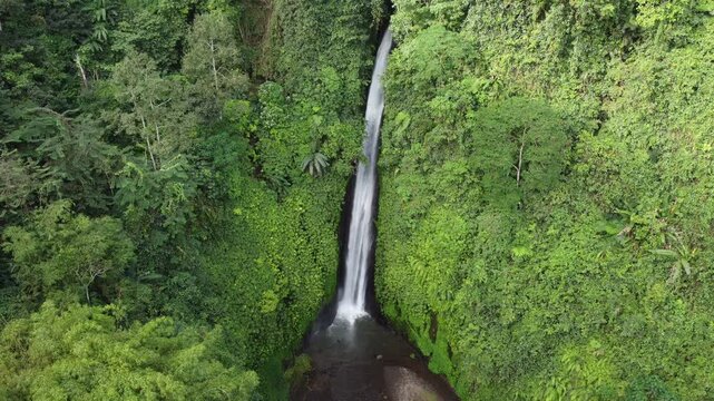 Cinematic aerial drone hovering in front of the complete Munduk Waterfall framed by tropical rainforest, Bali, Indonesia.