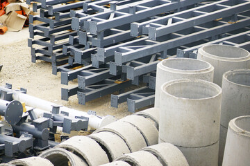 Gray painted steel structural frames alongside upright precast concrete manhole rings prepared for sequential installation. Reflects modular assembly planning and high-volume construction provisioning © tanyatorgonskaya