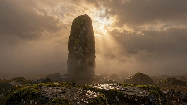 Ancient Standing Stone in Misty Landscape with Dramatic Sunlight