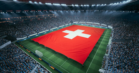 Fototapeta premium Professional Stadium Soccer Game Championship With Flag of Switzerland Spread Across the Pitch Before Football Match Start. Cheering Crowds of Fans Surround the Field. Aerial Wide Shot