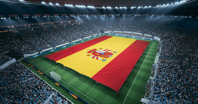 Professional Stadium Soccer Game Championship With Flag of Spain Spread Across the Pitch Before Football Match Start. Cheering Crowds of Fans Surround the Field. Aerial Wide Shot