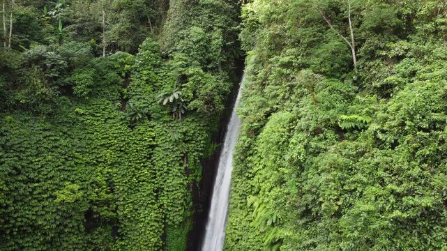 Cinematic aerial drone orbiting left around the main water drop of Munduk Waterfall in tropical jungle, Bali, Indonesia.