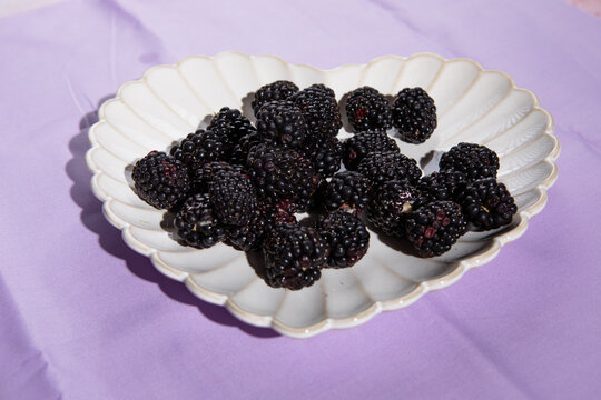 blackberries in heart plate on lilac cloth table top black blackberries