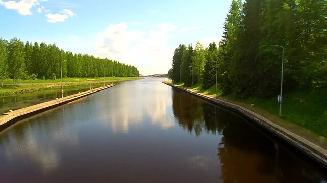Aerial drone view of canal in Aulanko Nature Reserve Hameenlinna Finland with straight waterway, tree lined walkways and calm reflective surface under blue sky