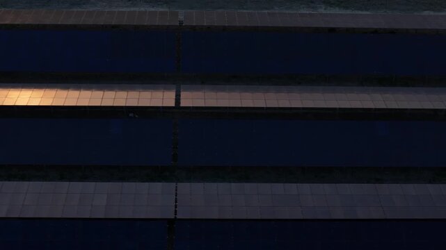Solar panel installation viewed from above with parallel arrays forming geometric patterns under warm sunset light in a renewable energy facility, drone top down pan shot