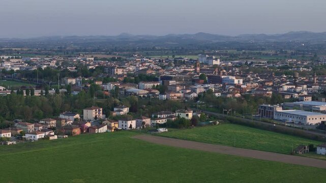 Fiorenzuola d&rsquo;Arda in PC Emilia Romagna Italy with town skyline featuring the Collegiata di San Fiorenzo church tower and distant Northern Apennines on the horizon within Po Valley land drone pull out