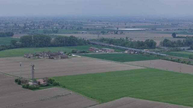 Trenitalia Frecciarossa high speed passenger train running parallel to Autostrada A1 near Fiorenzuola d&rsquo;Arda Piacenza Emilia Romagna Italy within Milan Bologna rail corridor, drone telephoto static